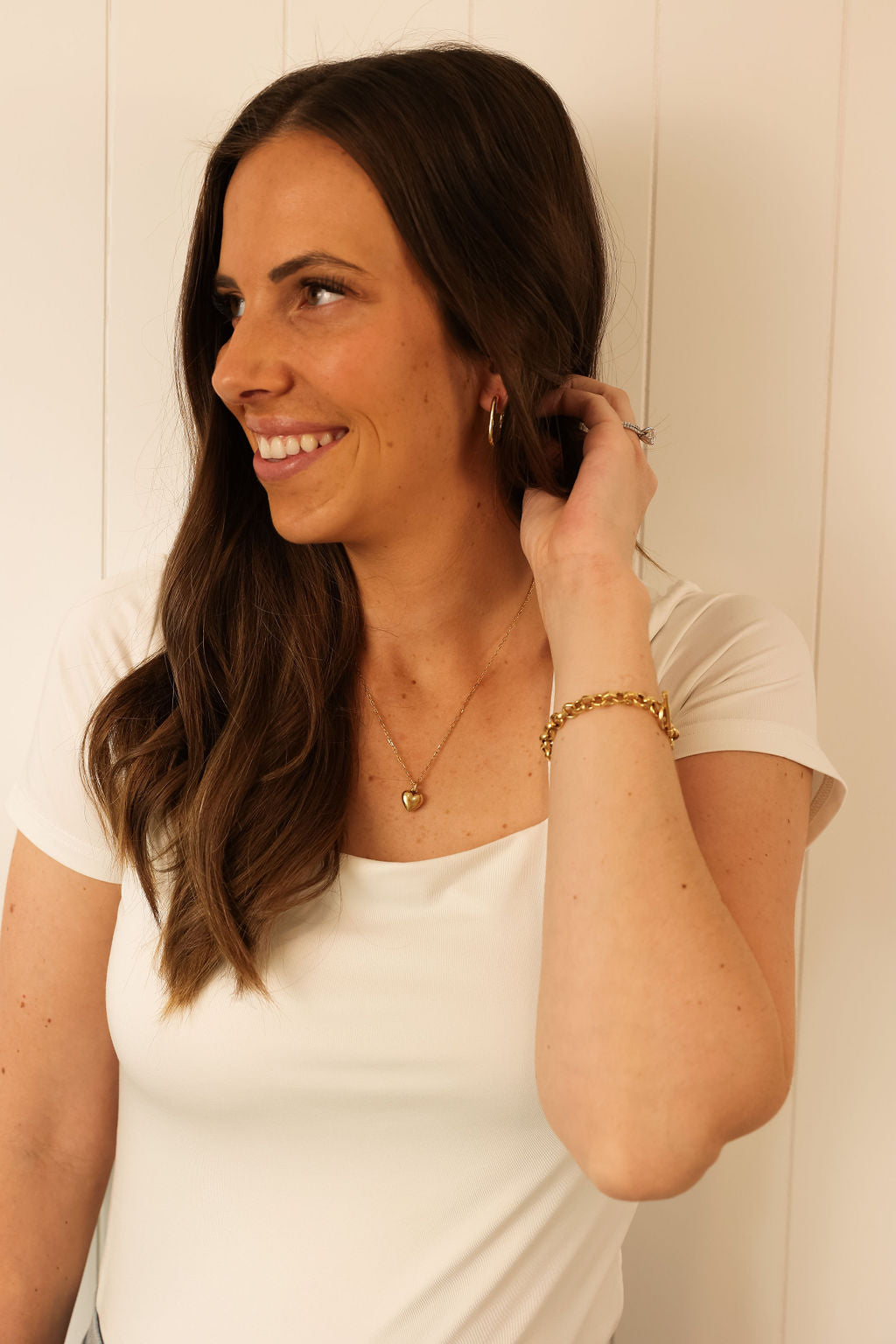 Model is wearing a gold chunky bracelet and a gold heart pendant necklace on a delicate chain.