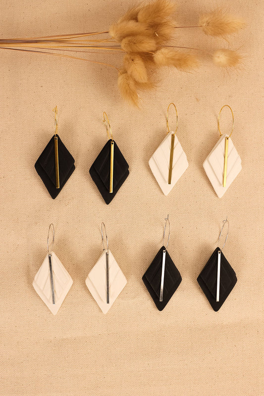 a close up view of black or white earrings with silver or gold hardware. earring shape is a diamond with a thin metal bar in the middle.