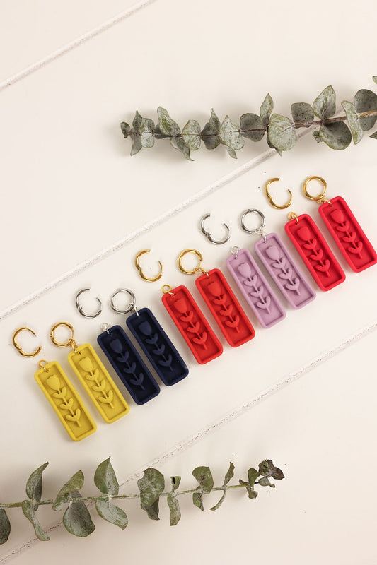 Set of colorful earrings on a light surface with green leaves.