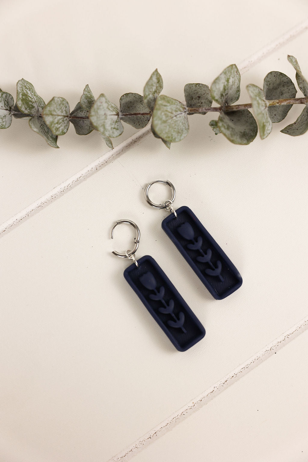 Navy blue earrings with a leafy branch on a light background