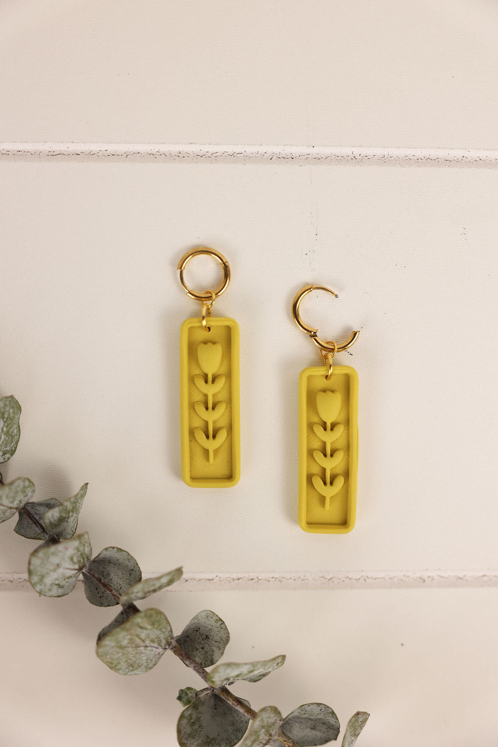 Two yellow earrings with leaf designs on a light background