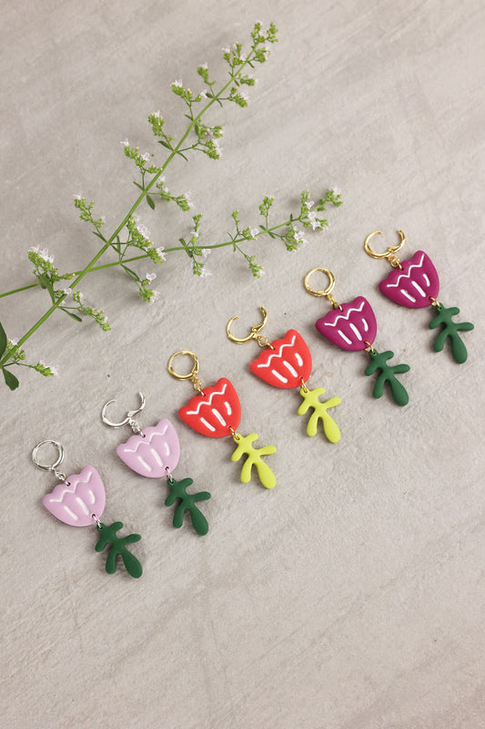 Colorful tulip-shaped earrings on a textured surface with a branch of flowers.