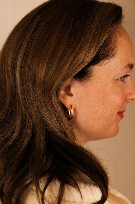 A side profile of a person wearing gold-plated square hoop earrings.