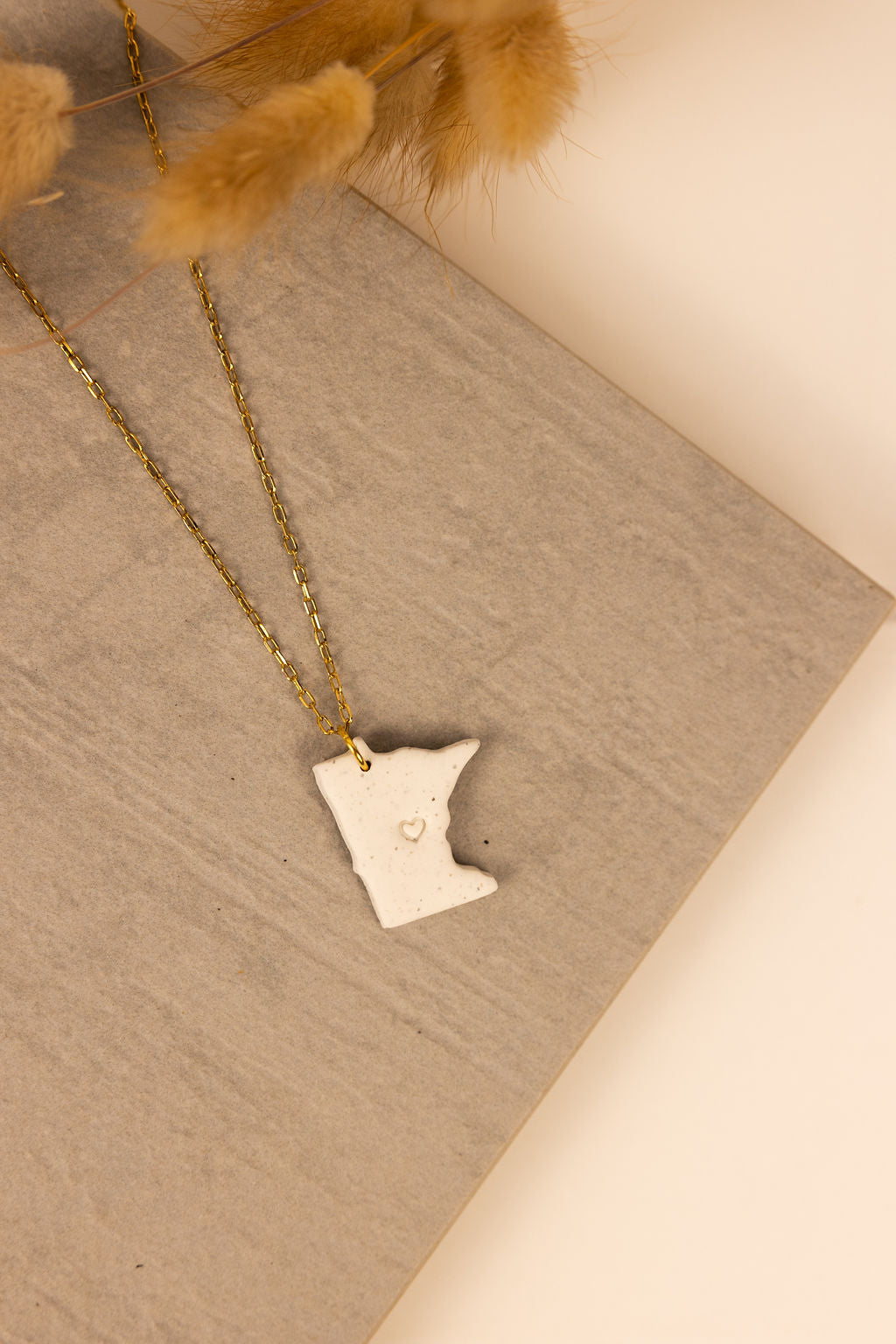 Handmade Minnesota shaped polymer clay necklaces with a gold chain. Each Minnesota pendent has a small heart stamped in the middle.