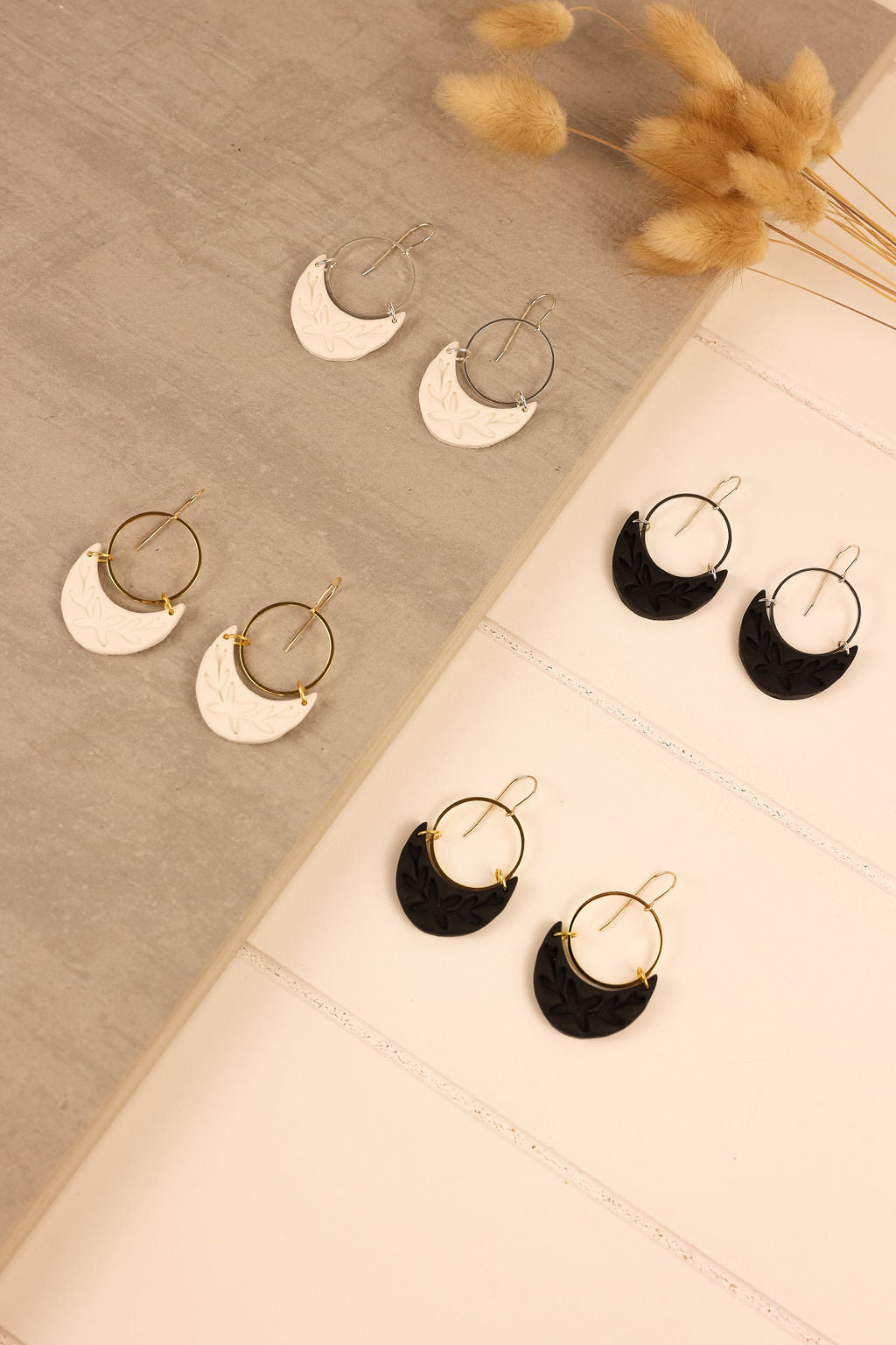 A display of dangle polymer clay earrings. Earrings have a moon shaped charm in either white or black.