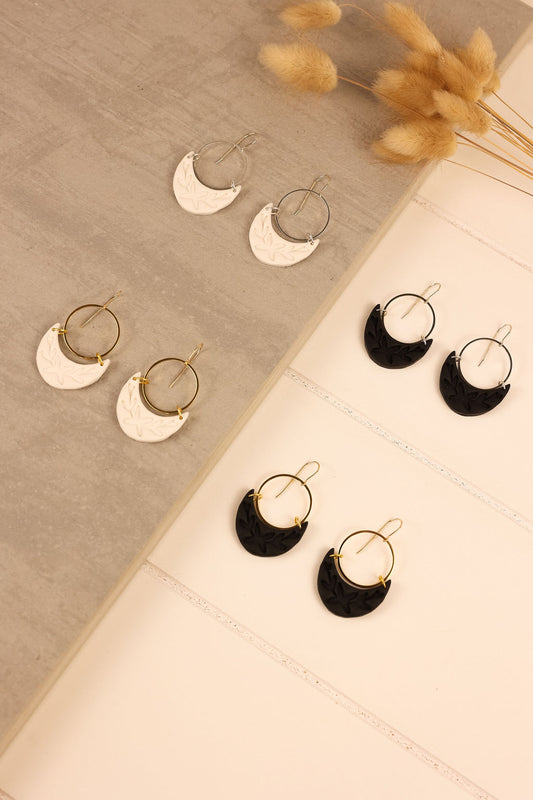 A display of dangle polymer clay earrings. Earrings have a moon shaped charm in either white or black.