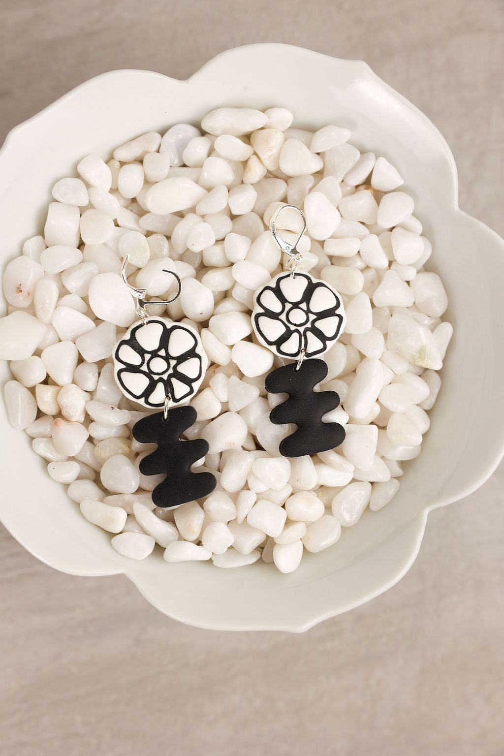 Black and white floral earrings on a bed of small pebbles in a decorative bowl.