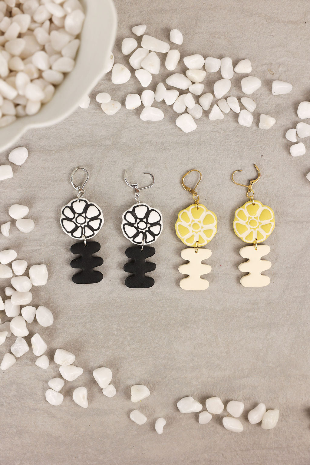 Set of four earrings with floral and geometric designs on a textured surface.