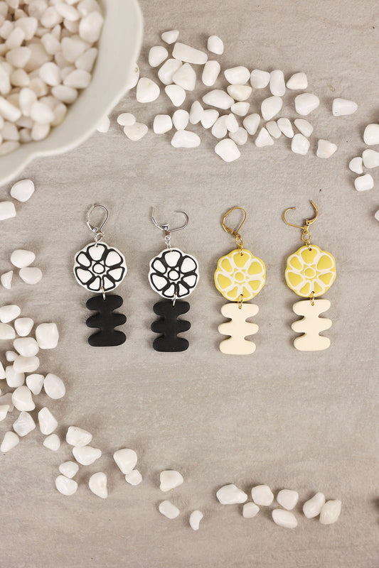 Set of four earrings with floral and geometric designs on a textured surface.