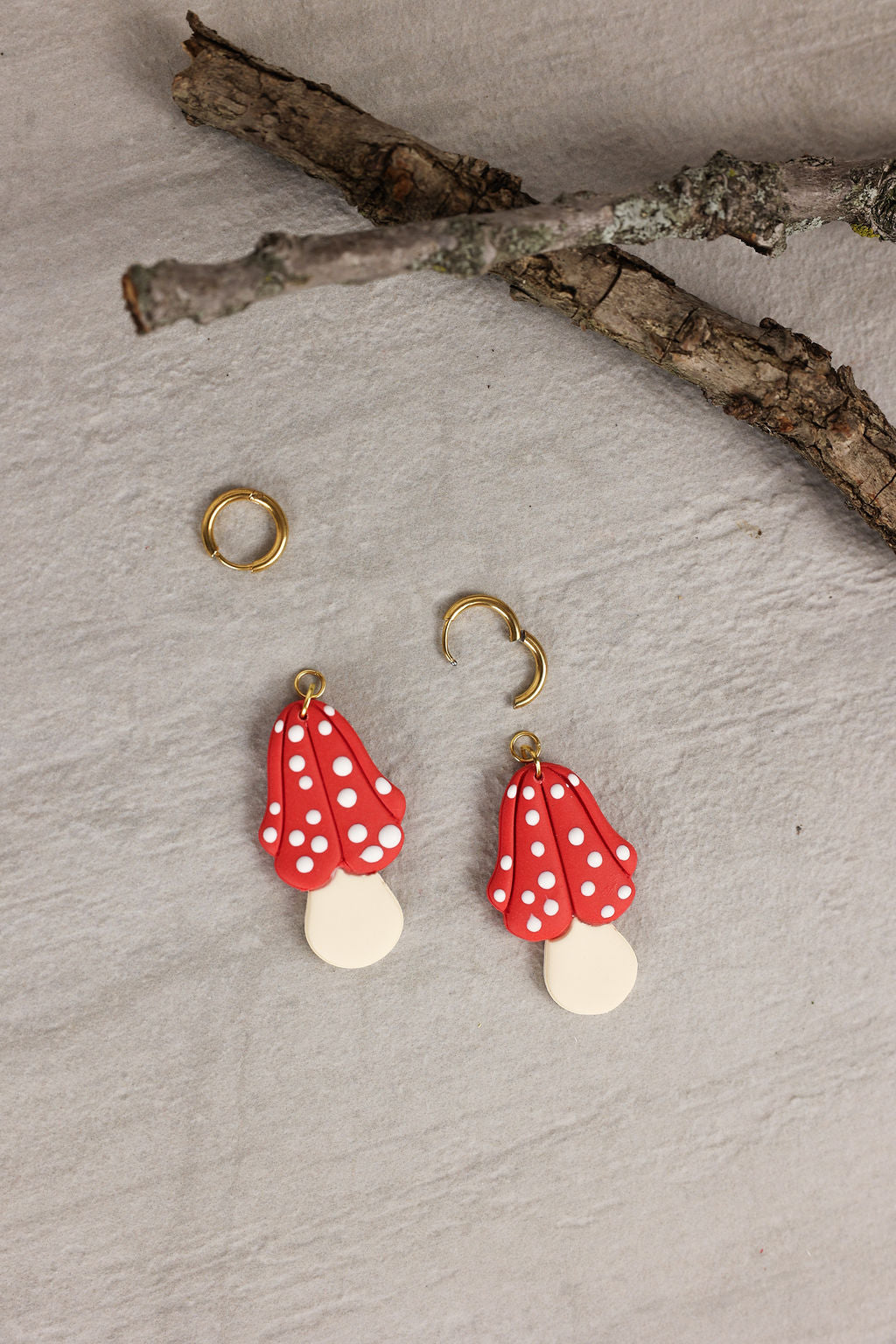 Red and white polka dot mushroom earrings with gold hardware on a textured surface. Image shows that the mushroom charms are removable.