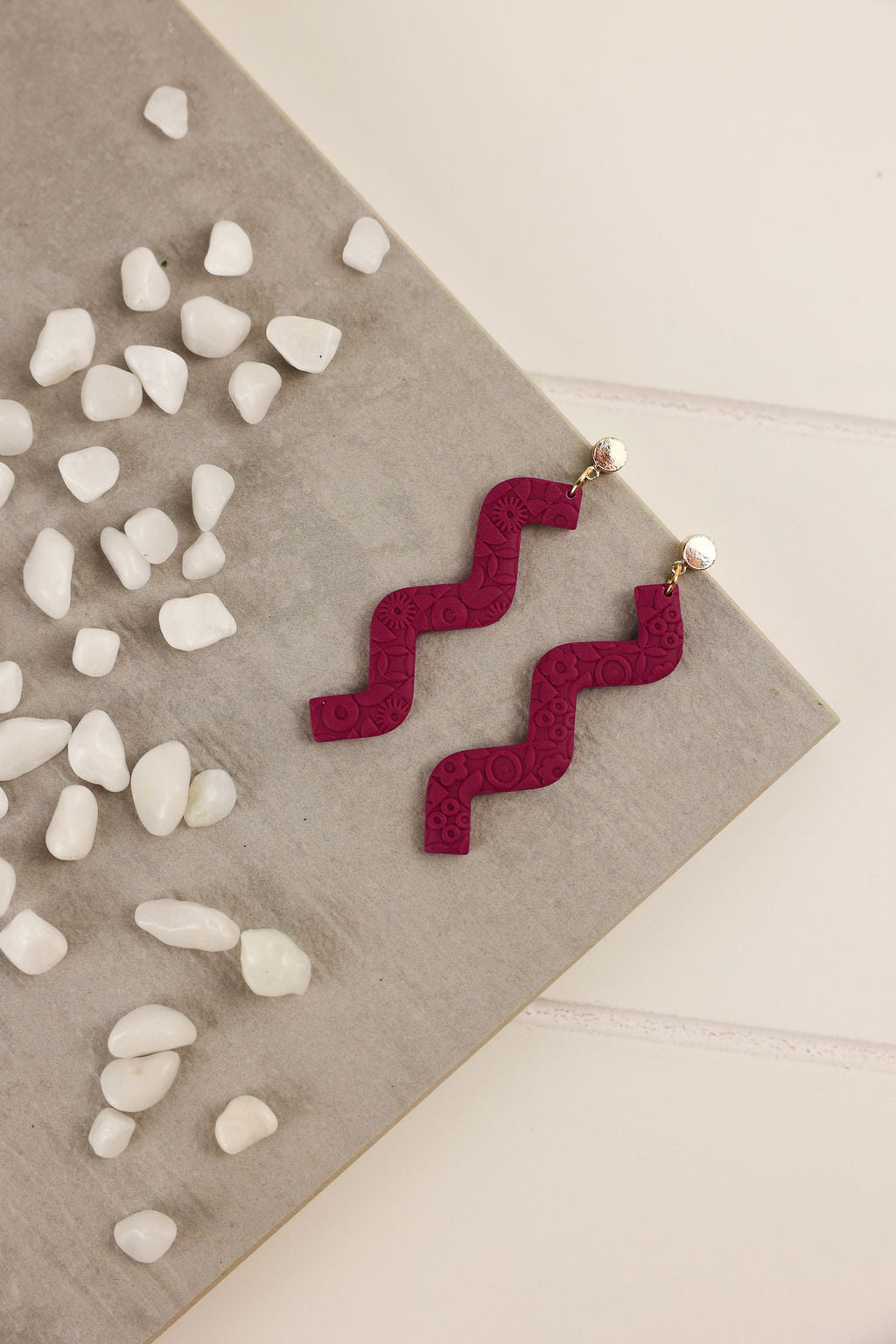 Amethyst color zigzag earrings on a neutral background with pebbles