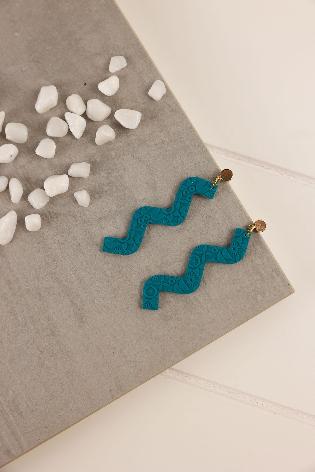 Dark Teal zigzag earrings on a gray surface with small white stones.