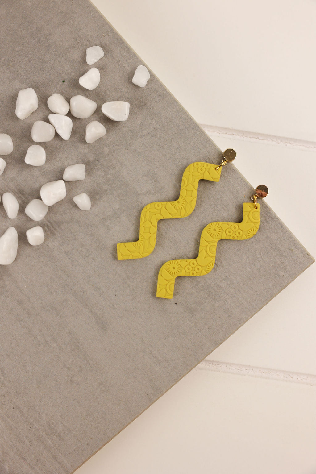 mustard Yellow zigzag earrings on a textured surface with small white stones.