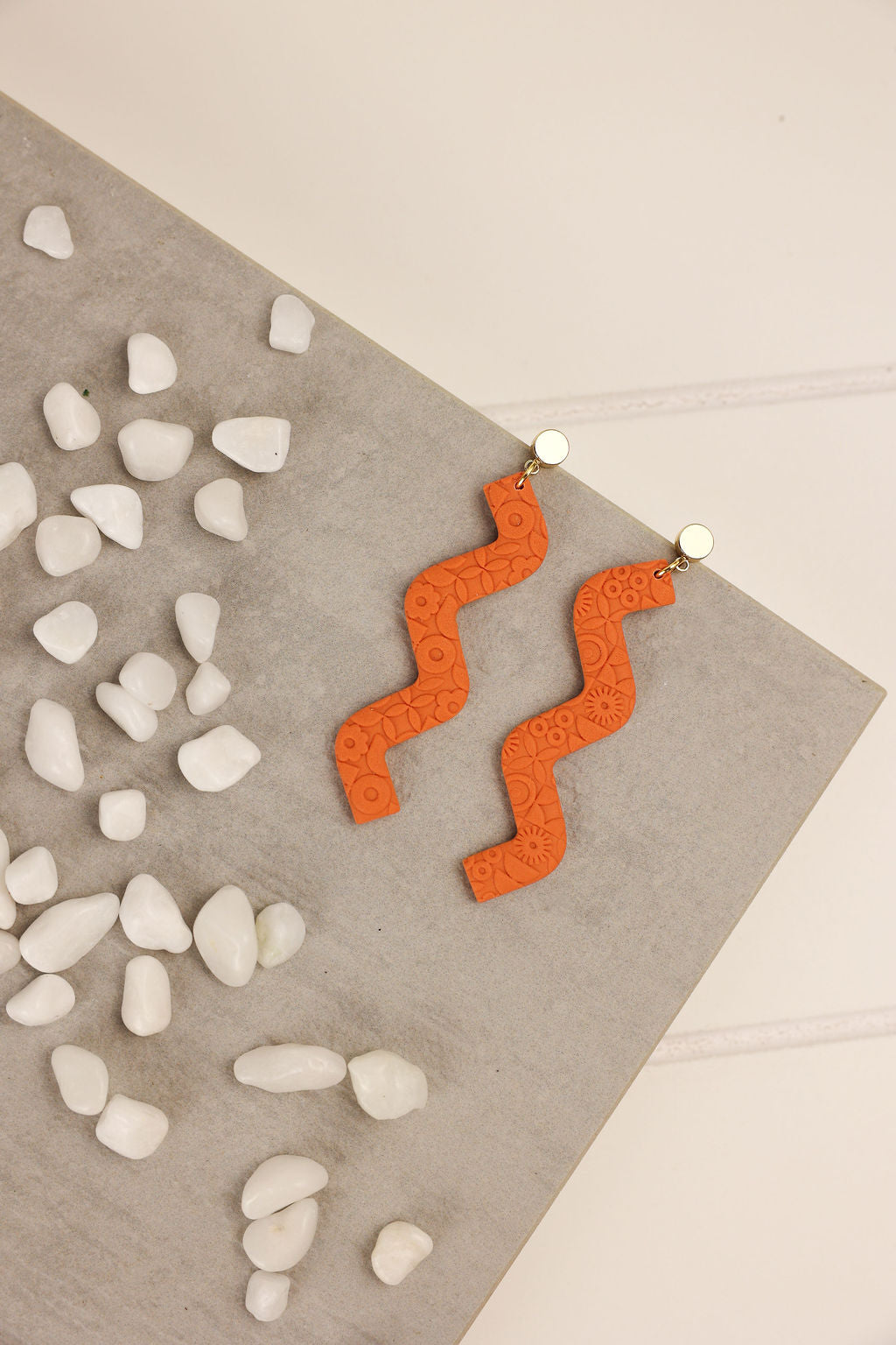 Orange zigzag earrings on a gray surface with white stones