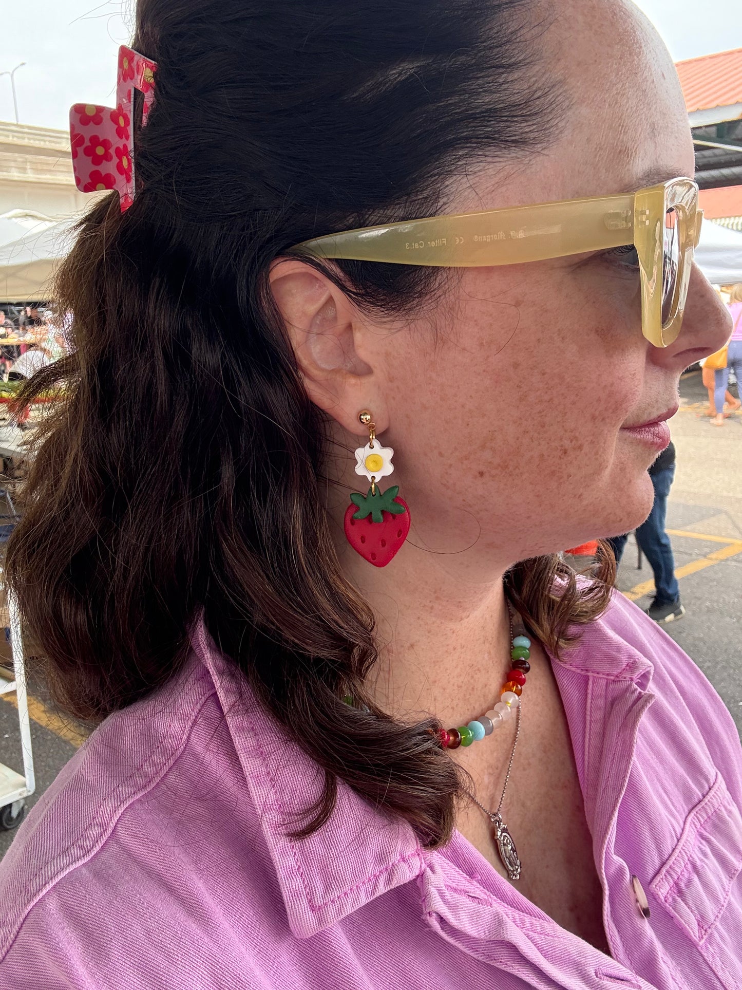 Woman wearing strawberry earrings and a colorful necklace at the Minneapolis Farmer's Market.