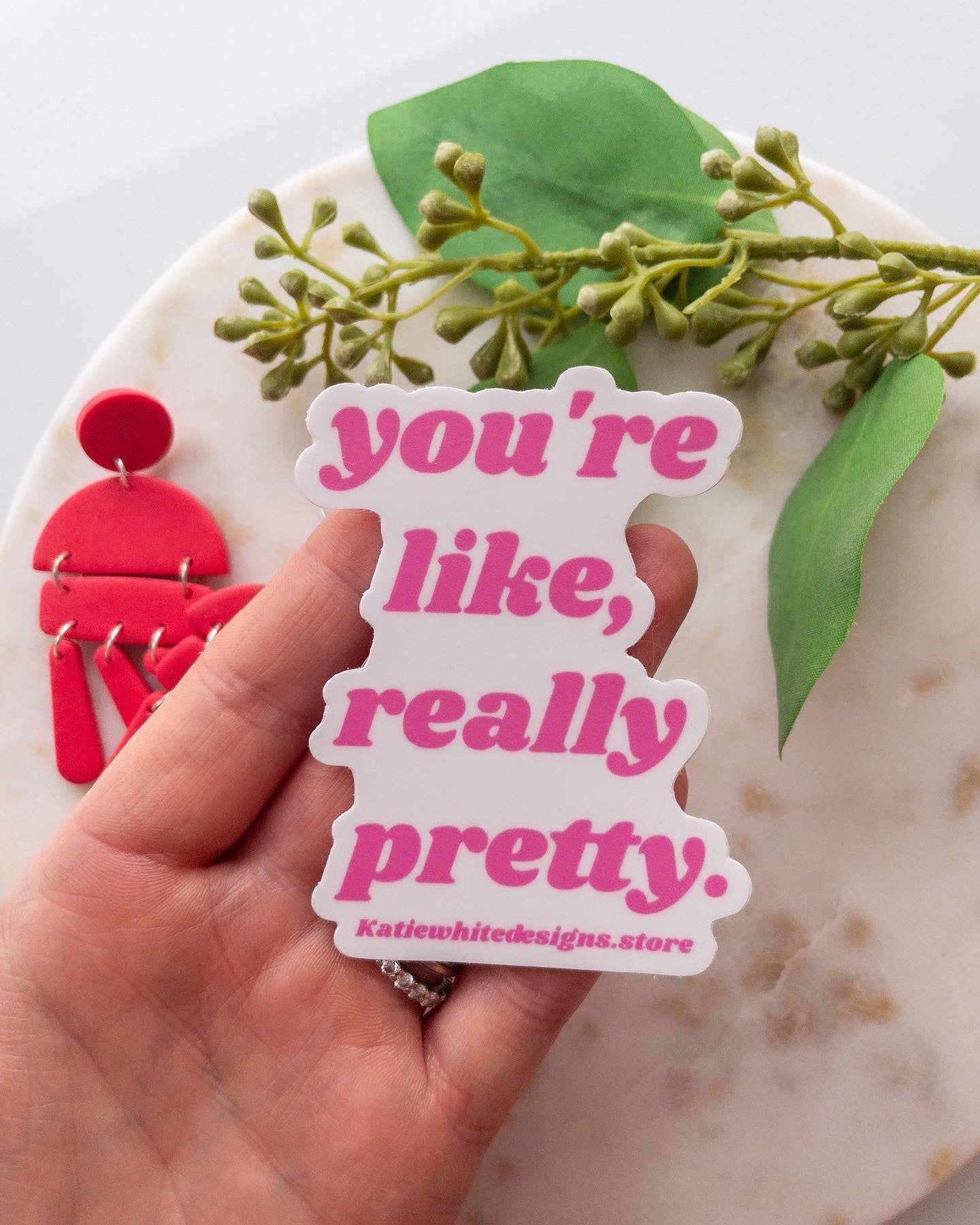 Pink sticker being held in hand. Sticker says "You're like, really pretty."