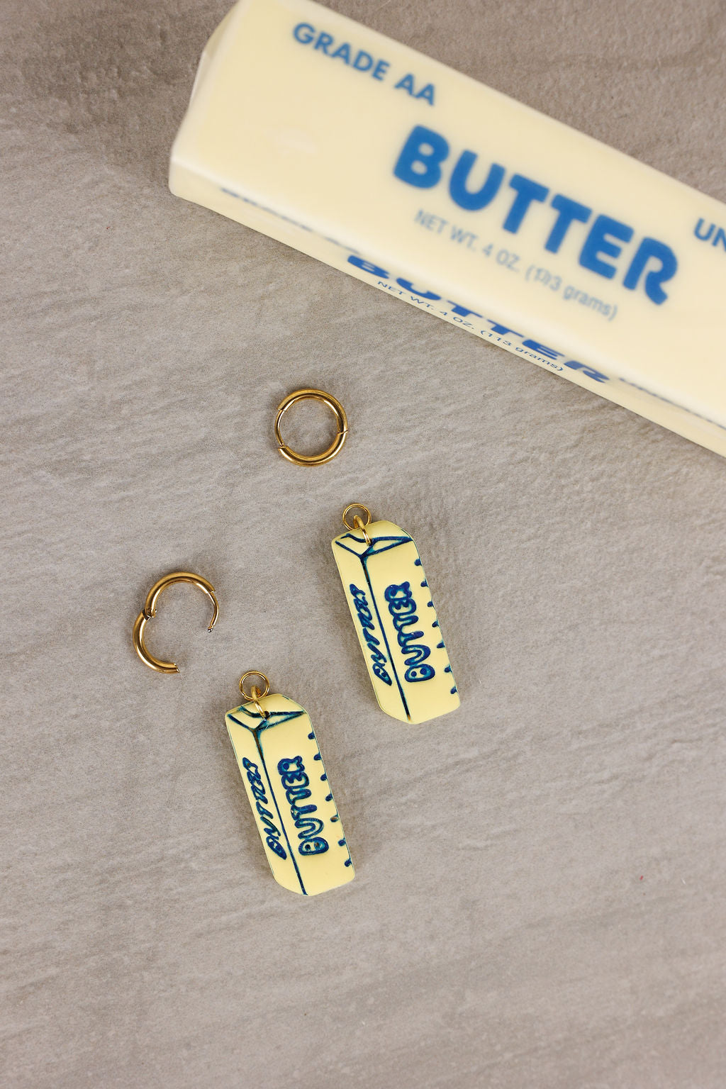 Butter container-shaped earrings with gold hooks on a gray surface.