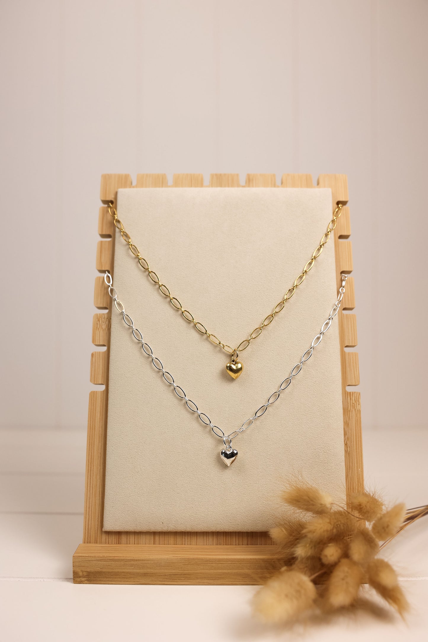 silver and gold heart charm necklace on a chunky chain on a wooden display