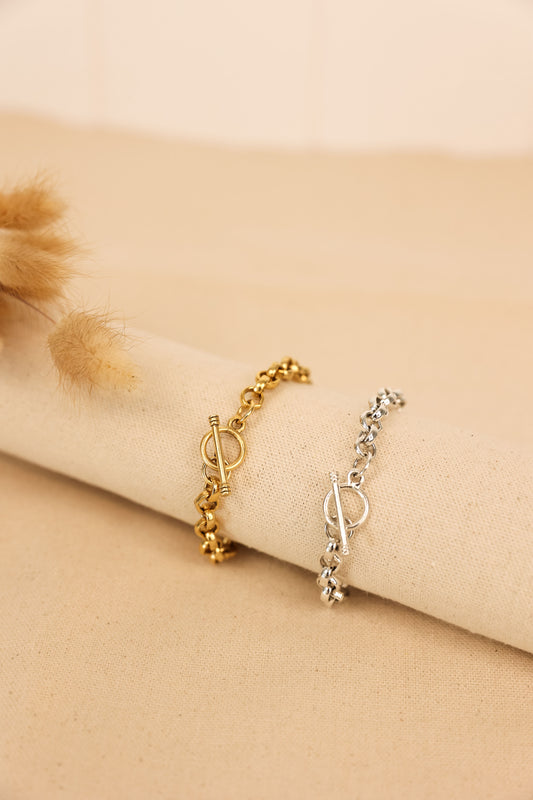 Two chunky bracelets with toggle clasps, one in gold and the other in silver, displayed on a beige surface.