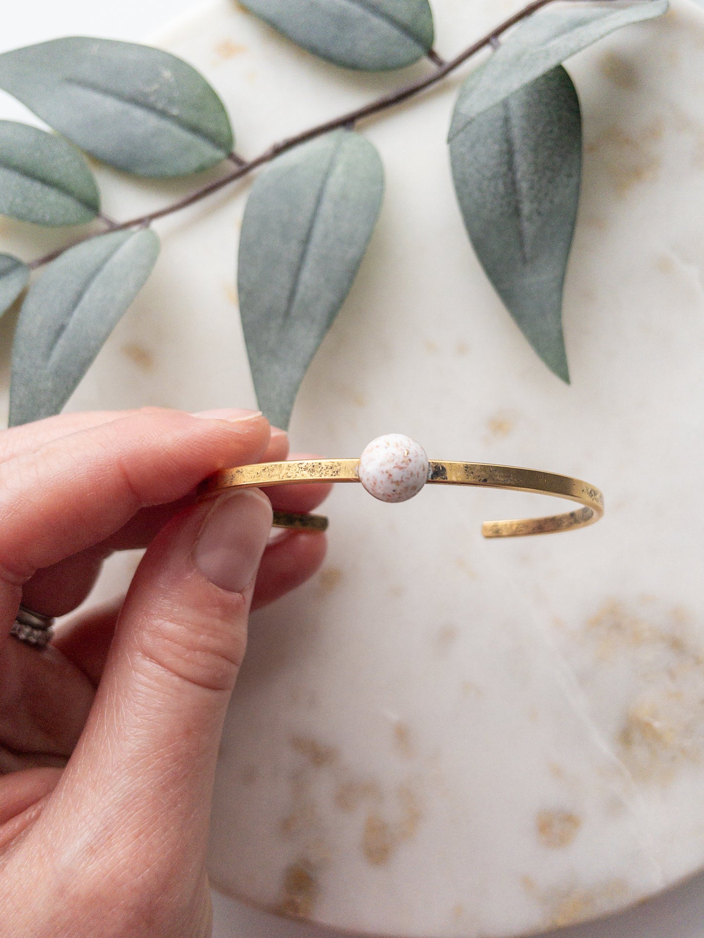 Gold cuff bracelet with granite colored clay bead set into the middle of the bracelet.