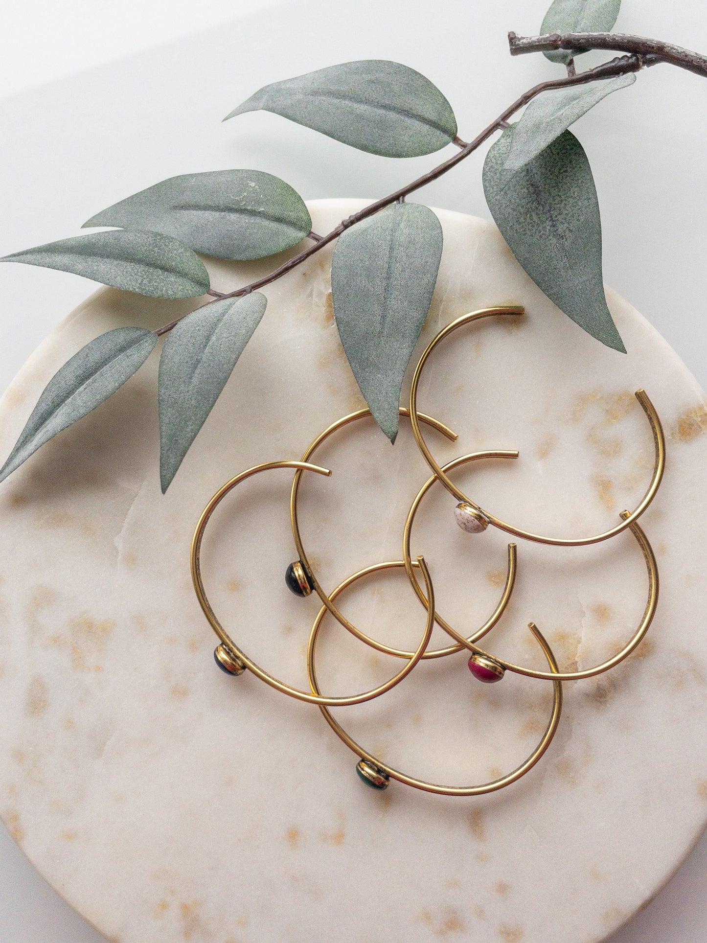 Gold and silver cuff bracelets with a colored clay bead set into the middle of the bracelet.