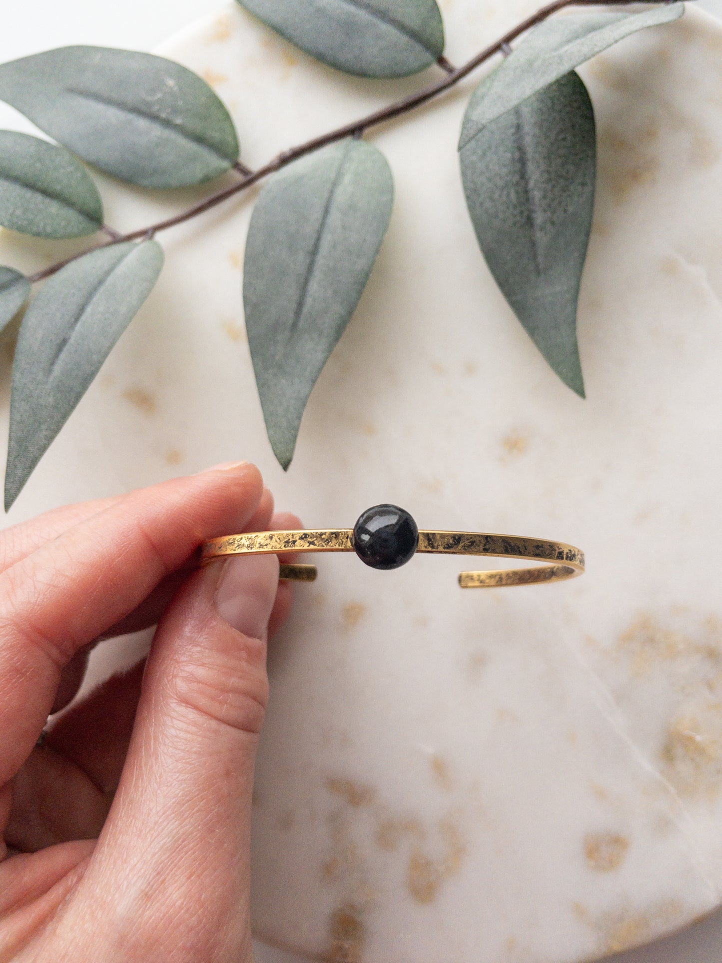 Gold cuff bracelet with black colored clay bead set into the middle of the bracelet.