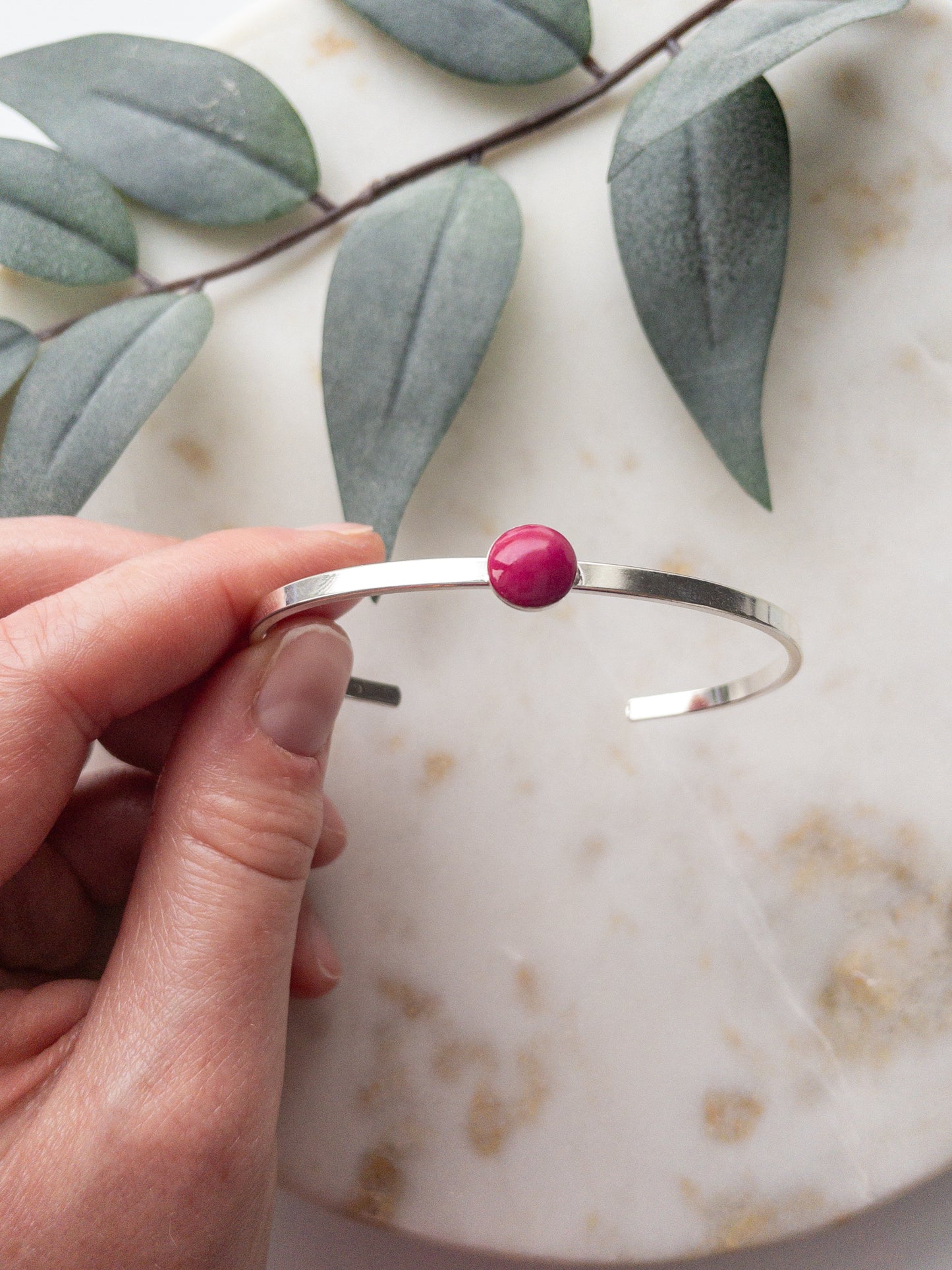 Silver cuff bracelets with a rose colored clay bead set into the middle of the bracelet.
