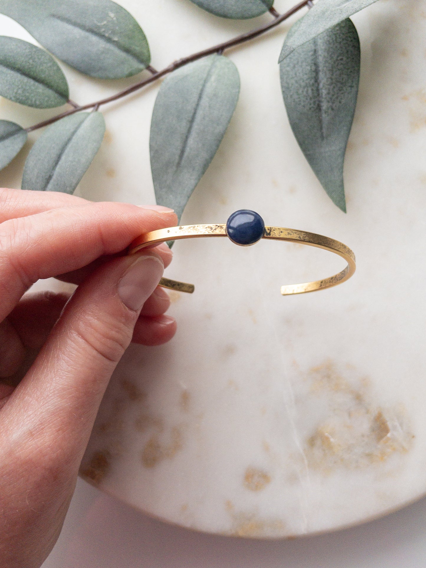 Gold cuff bracelets with a navy colored clay bead set into the middle of the bracelet.
