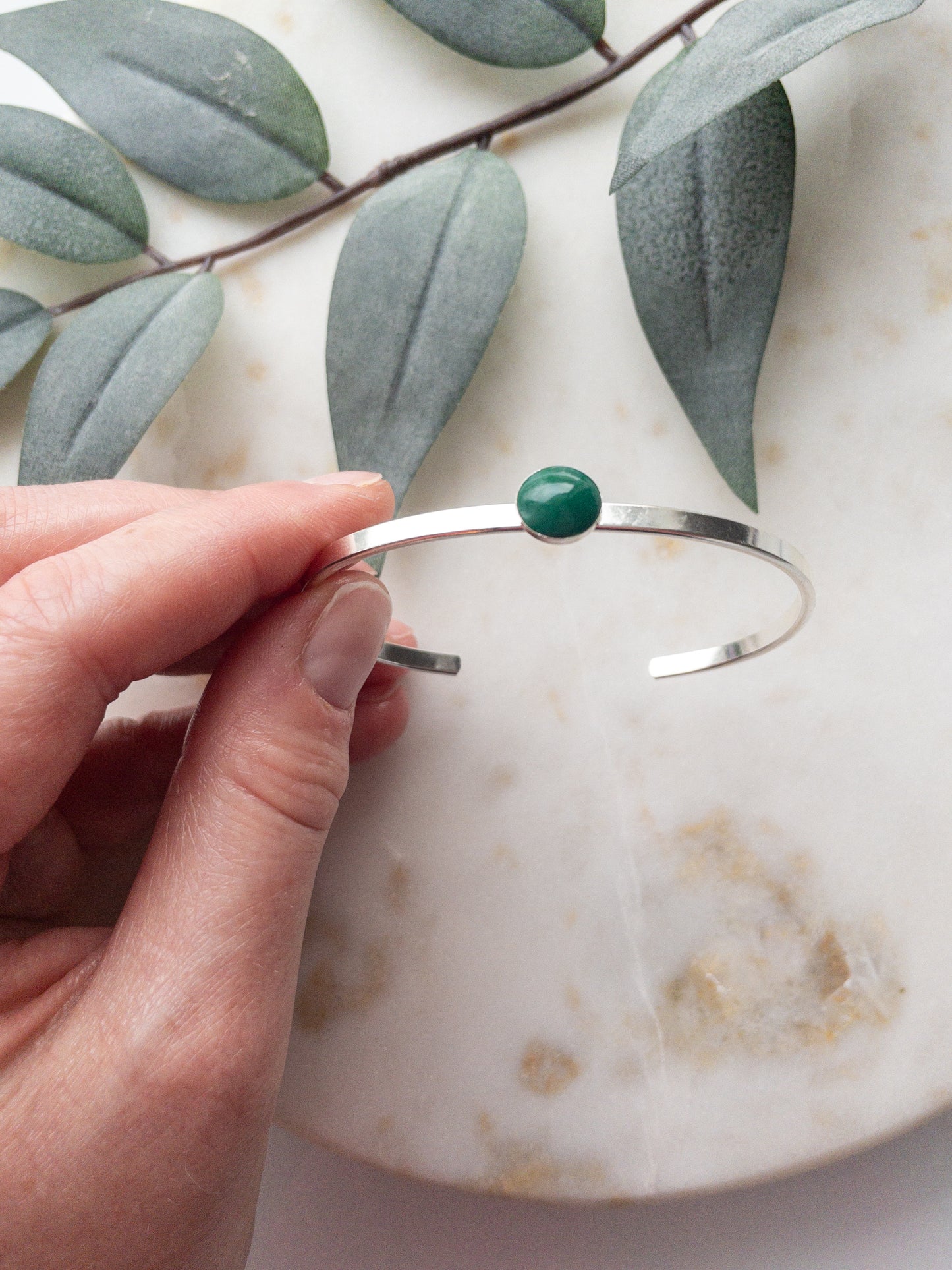 Silver cuff bracelet with emerald colored clay bead set into the middle of the bracelet.