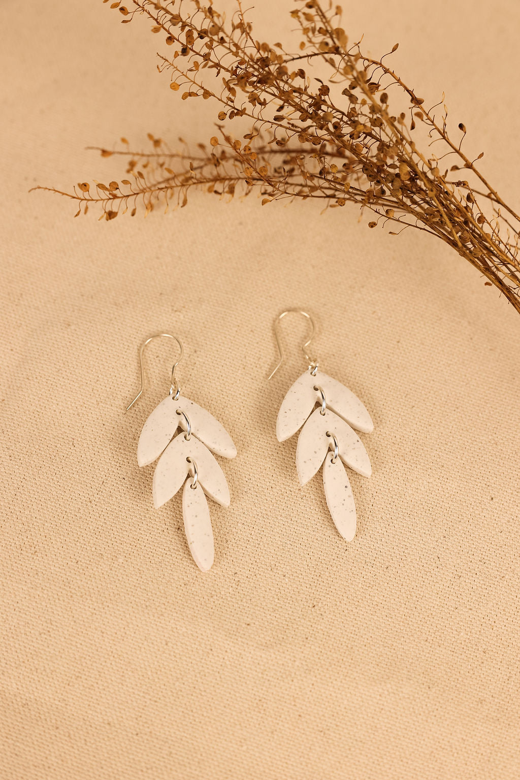 These earrings are made of white polymer clay. They have a leaf design and dangle from the ear.