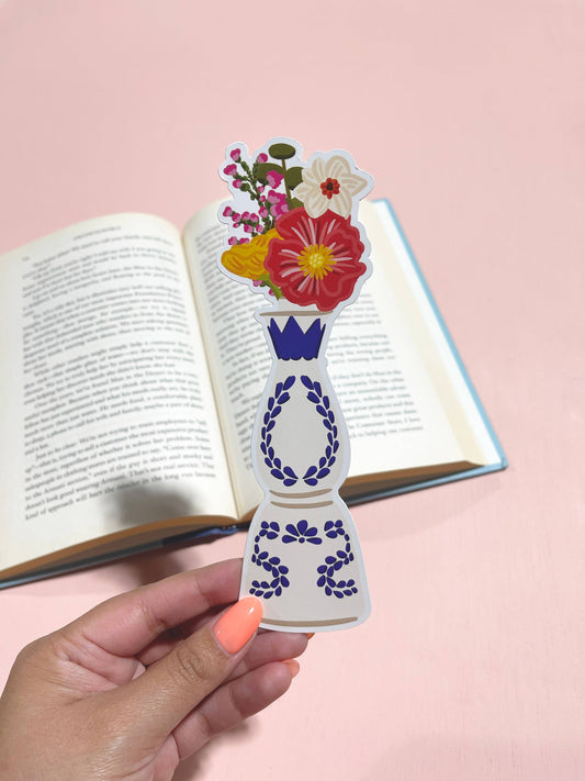 A die-cut floral bookmark held between the pages of an open book, featuring colorful flowers on top and a blue patterned design at the bottom.