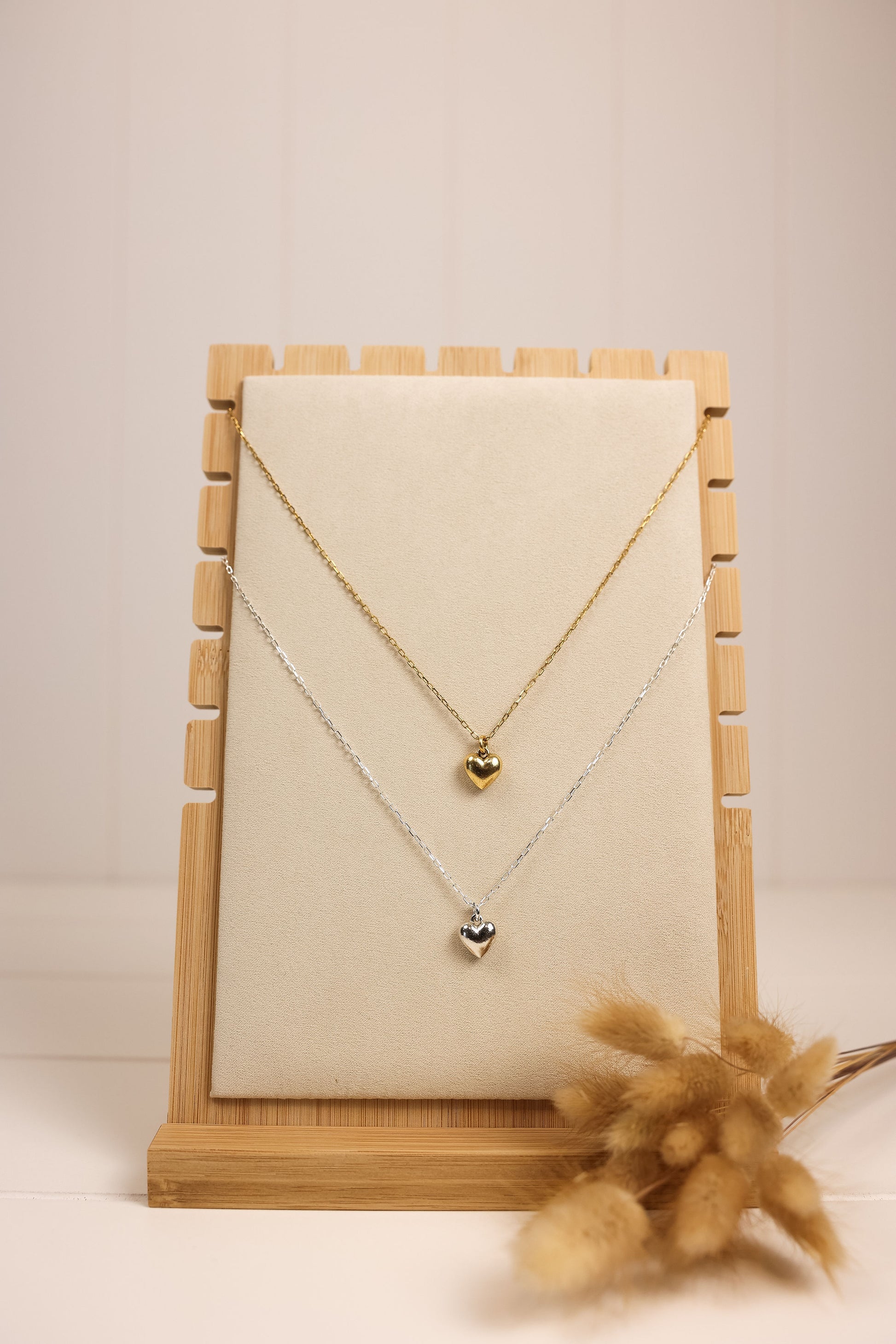 heart charm necklace on a thin metal chain. gold and silver options are displayed on necklace stand. 
