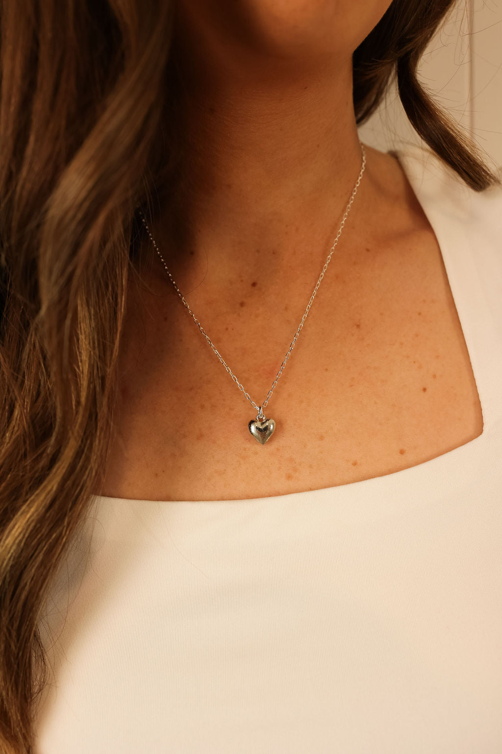 Delicate heart necklace in silver worn on  a model. 