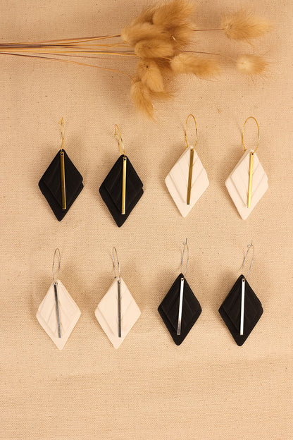 a close up view of black or white earrings with silver or gold hardware. earring shape is a diamond with a thin metal bar in the middle. 