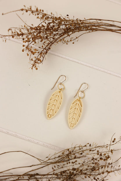 Ivory colored leaf earrings on a light background with dried branches.