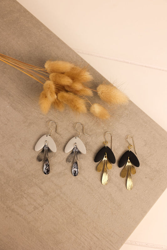 A collection of clay earrings in black and gray displayed on a slate surface. 