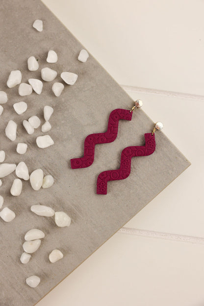 Amethyst color zigzag earrings on a neutral background with pebbles