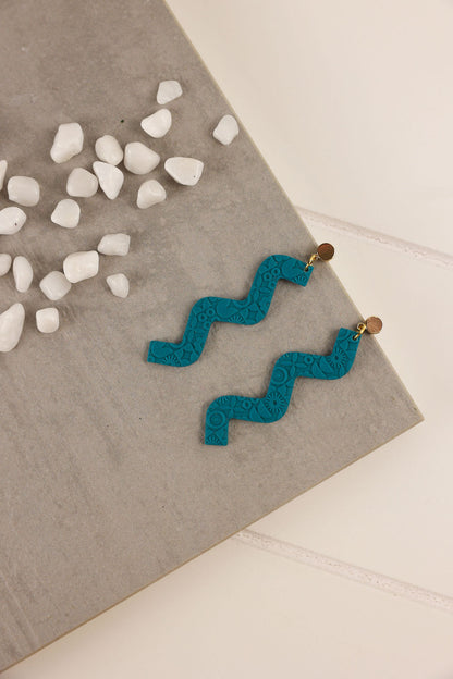 Dark Teal zigzag earrings on a gray surface with small white stones.