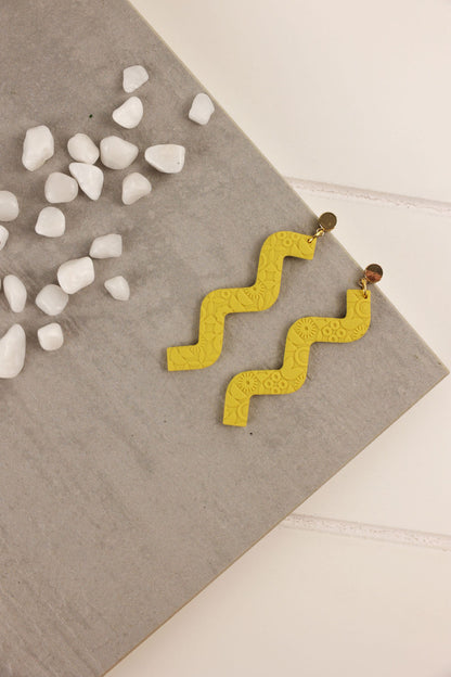 mustard Yellow zigzag earrings on a textured surface with small white stones.