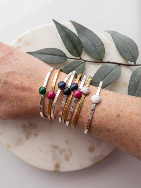 Gold and silver cuff bracelets with a colored clay bead set into the middle of the bracelet. 