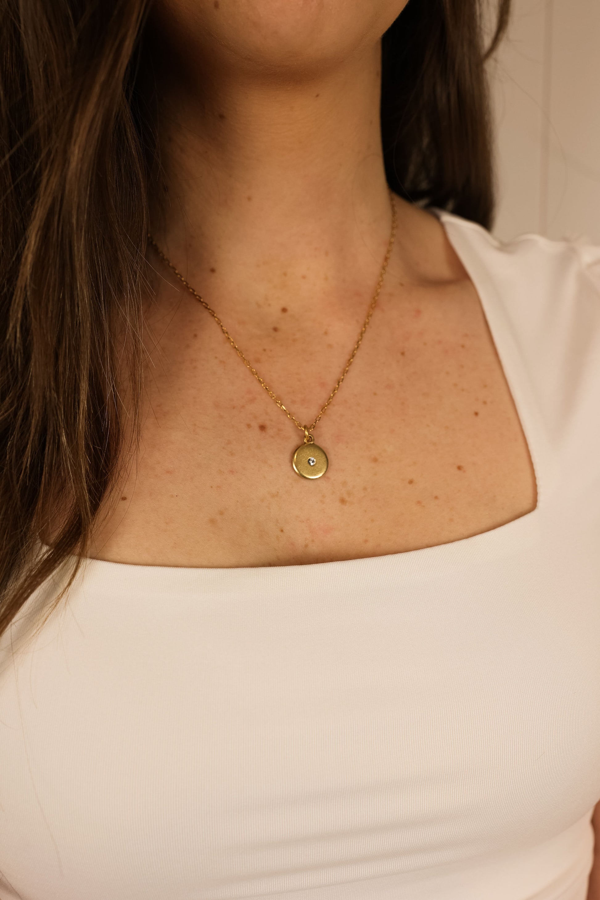 Gold disk necklace on model. Disk pendant has a small crystal in the middle. 