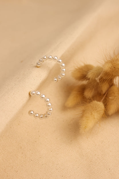 pearl hoop earrings displayed on textured cloth. 